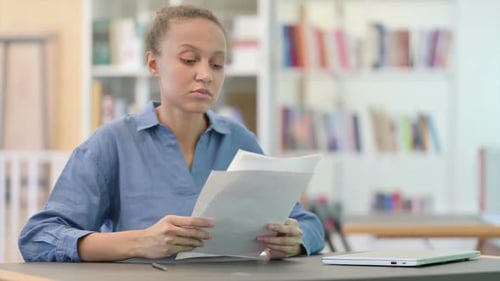 Young African Woman Reading Documents in Library