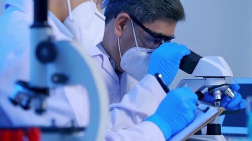 Asian scientists doing some research and looking through a microscope in laboratory.