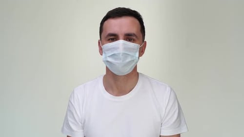 Un jeune homme effrayé portant un masque médical s'étouffe devant la caméra.