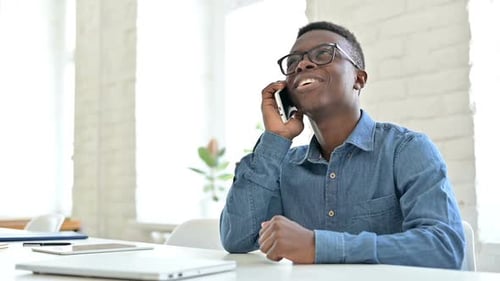 Smiling Young African Man Talking on Smartphone in Office