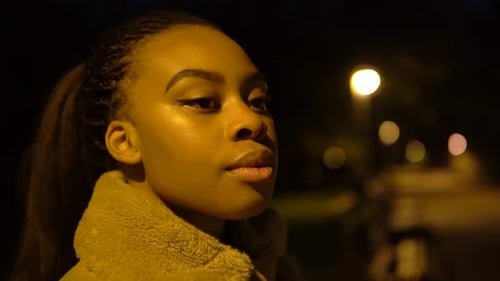A Young Black Woman Looks Around in a City Park at Night Face Closeup