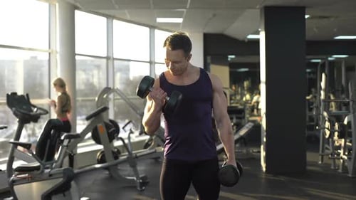 Männlicher Bodybuilder beim Gewichtheben, Hantel-Curls machen, Morgentraining im Fitnessstudio