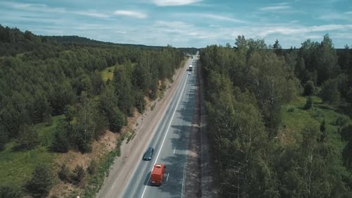 Luftaufnahme eines Intercity-Highway mit Verkehr durch einen grünen Wald an einem hellen, sonnigen Tag