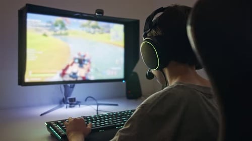 Young boy sitting in front of a computer, playing a game wearing a headset