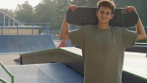 Young Man Smiling Holding Skateboard in Skate Park
