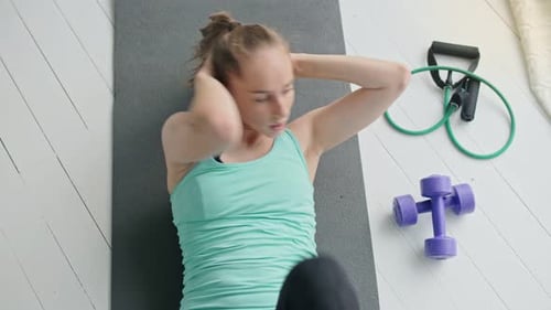 Draufsicht auf ein attraktives junges Mädchen, das zu Hause auf der Fitnessmatte trainiert und Übungen für Bauchmuskeln macht