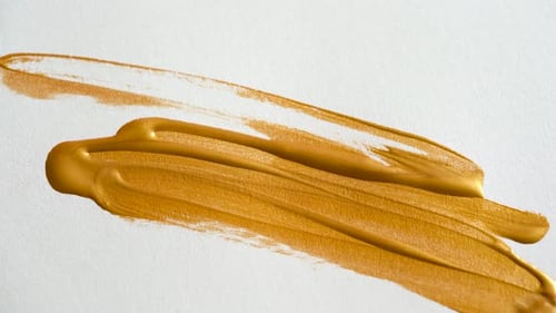 Drawing with a Paintbrush on White Paper with Bright Golden Acrylic Paint Close Up