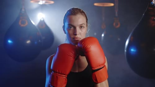 Portrait of Woman Kickboxer Ready to Punch Wearing Red Boxing Gloves Standing on the Sport Gym