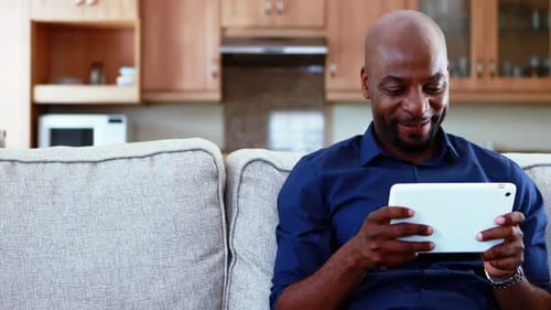 Bald Man Uses Tablet on Couch at Home