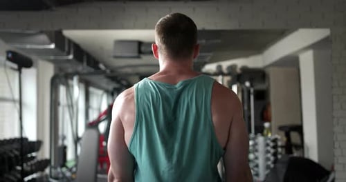 A man in a gym with his back doing an exercise for biceps raises a barbell in front of him