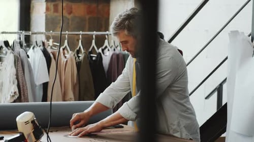 Male Tailor Drawing with Chalk and Cutting Fabric in Sewing Studio