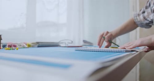 Person Drawing in a Notebook at a Table