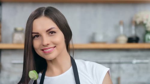 Smiling Woman with Cucumber Slice in Modern Kitchen