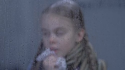 Kleines Mädchen niest und schaut durch regnerisches Fenster in die Kamera
