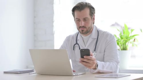 Young Doctor Using Smartphone While Using Laptop in Clinic