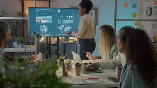 Office Worker Pointing at Digital Screen and Discussing Marketing Ideas in Boardroom at Night