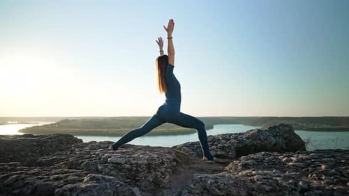 Sporty Woman in Blue Costume Practicing Yoga on High Rock Above Water