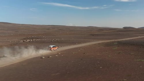 Tracking of Two Colour SUV Car Driving Fast on Dusty Road in Barren Volcanic Landscape