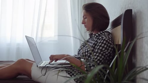 Woman Works on Laptop Sitting on Bed Indoors