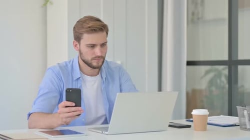 Man Using Phone While Working on Laptop