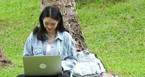Female Student Sitting On Grass In Park And Using Laptop Computer
