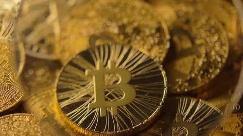 Main de personne avec loupe au-dessus de pièces fabriquées par Bitcoin Macro