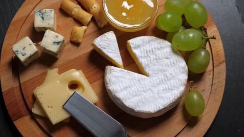 Sliced Cheese,nuts, Grape, Honey and Knife on Wooden Platter. Rotate