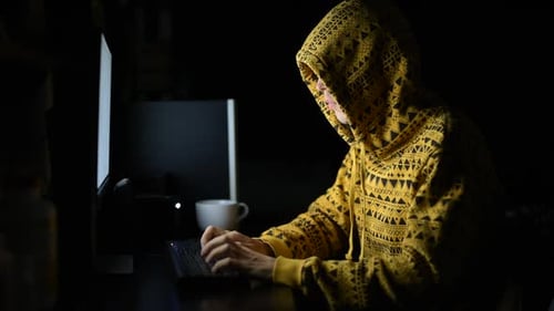 Jeune homme portant un sweat à capuche en tant que hacker utilisant un téléphone et un ordinateur dans le noir