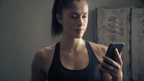Young Woman Using Phone in Gym Locker Room