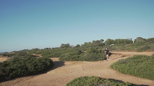 Woman Runs Along Ocean Cliff Trail on Sunny Day