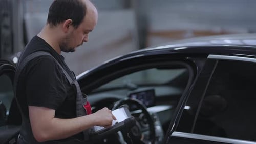 Porträt Ein Mechaniker in einer Autoservice-Nahaufnahme hält ein Tablet in den Händen und drückt auf den Bildschirm