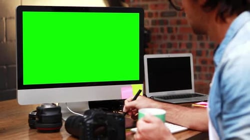 Man Working at Desk with Green Screen Monitor