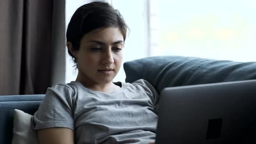 Young Woman at Home Sitting on a Couch Works on a Laptop Computer. Girl Using Computer