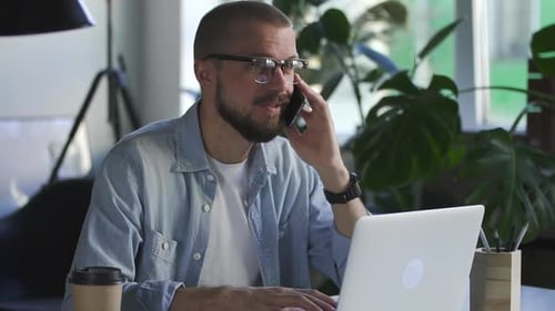 Handsome Man Accountant Talking on the Phone with Smile in Office with Laptop Computer