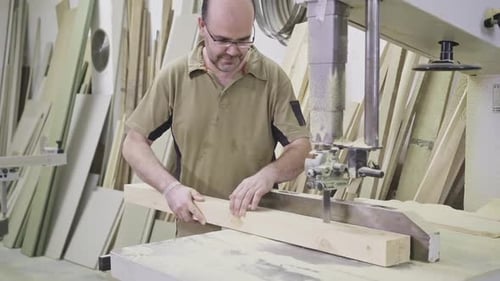 Man Cutting Wood with a Saw in a Workshop