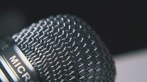 Man Taps on Shining Microphone By Finger on Dark Background