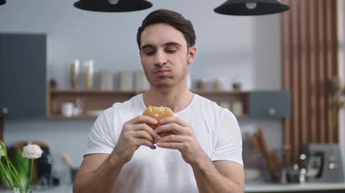 Young Man Enjoys Burger in Kitchen