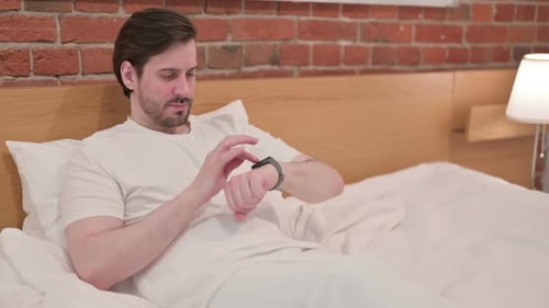 Man in Bed Using Smartwatch in Bedroom
