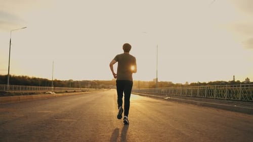 Young Sportsman is Running Alone in Summer Morning or Evening Rear View of Male Jogger