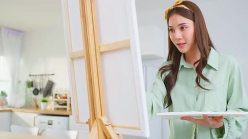 Asian young talented woman artist coloring on painting board in house.