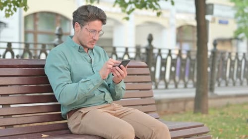 Man Browsing on Smartphone while Sitting on Park Bench