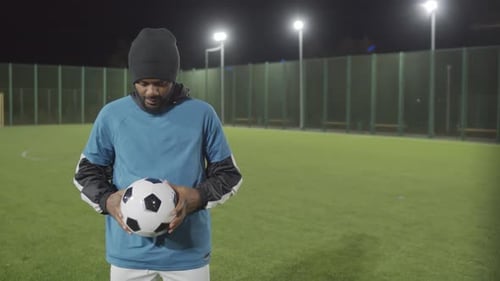 Man Holding Soccer Ball on Artificial Turf Field at Night