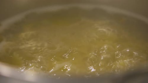 Water boiling and bubbling in a stainless pot in the kitchen, steam, vapor, close up shot