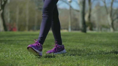 Slim Female Legs in Black Leggings Walking on Grass in Park