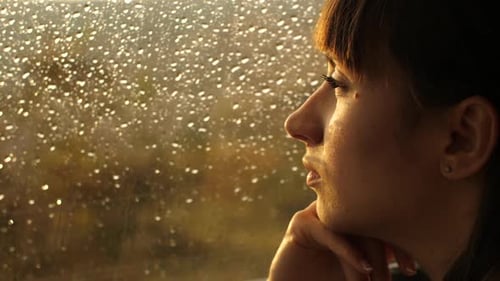 Frau sitzt allein am Fenster mit Regentropfen