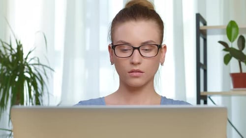 Focused young woman in glasses is working on a laptop.