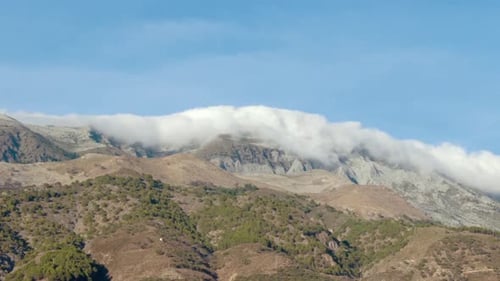 Timelapse of Billowing Clouds Rolling Over the Top of a Mountain.