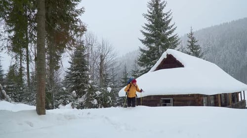 Adventurous Hiker Snowshoeing Past Cabin in Winter Landscape