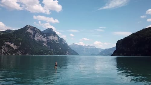 Orbiting aerial shot around a stand up paddler on a yellow stand up paddle, sup with a straw hat in
