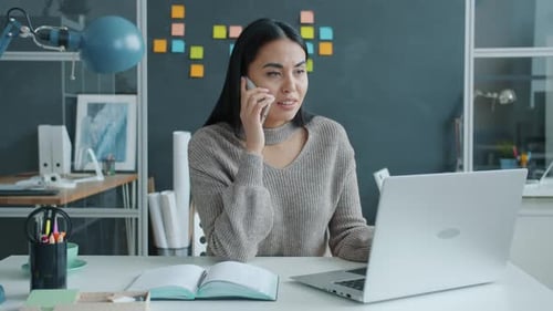 Happy Mixed Race Woman Talking on Mobile Phone Getting Good News Using Laptop in Office